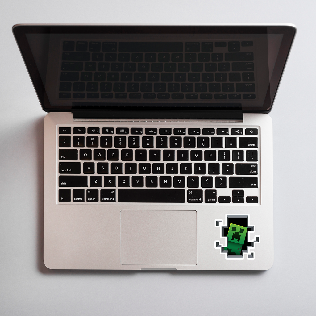 Laptop with a Minecraft creeper sticker on a light gray background