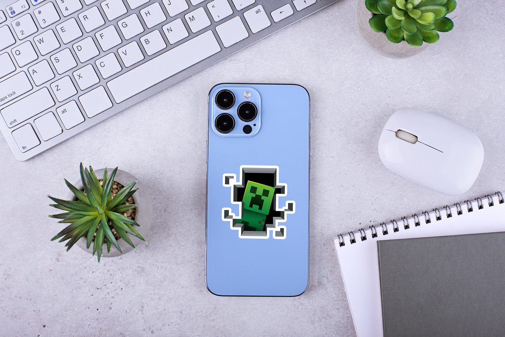 Blue phone case with a Minecraft Creeper sticker on a desk with keyboard and mouse.